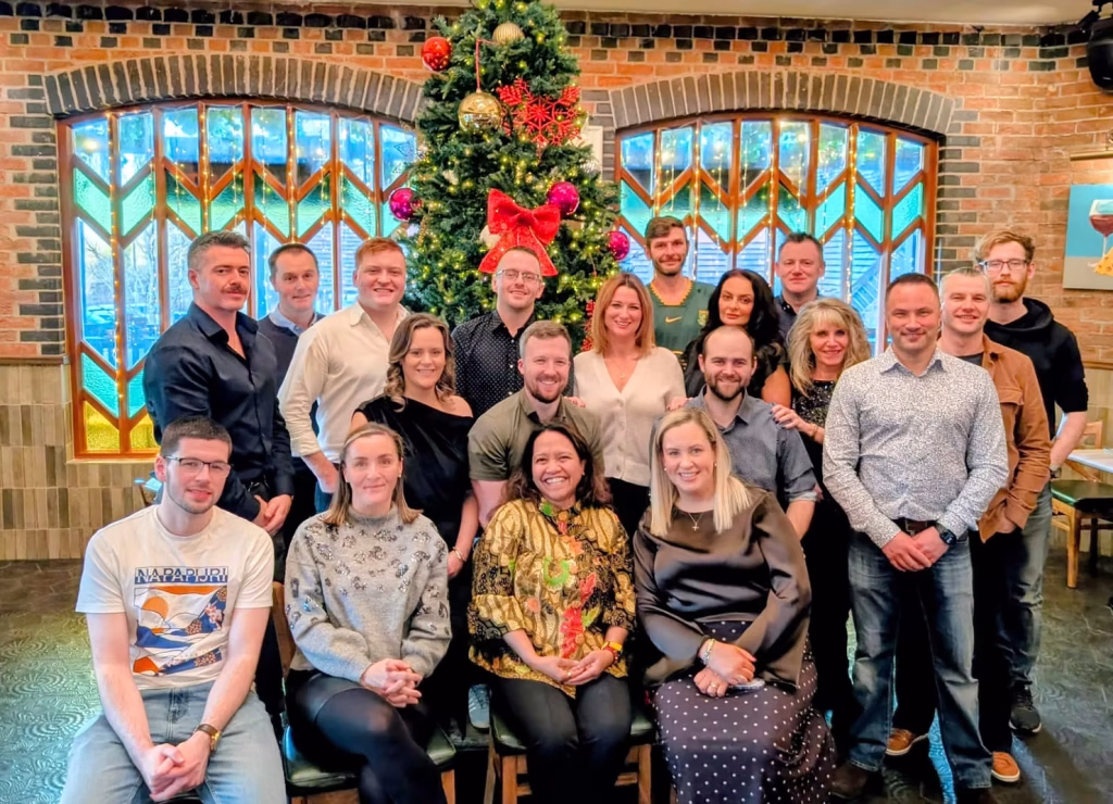 Team photo of employees gathered indoors in front of a decorated Christmas tree.