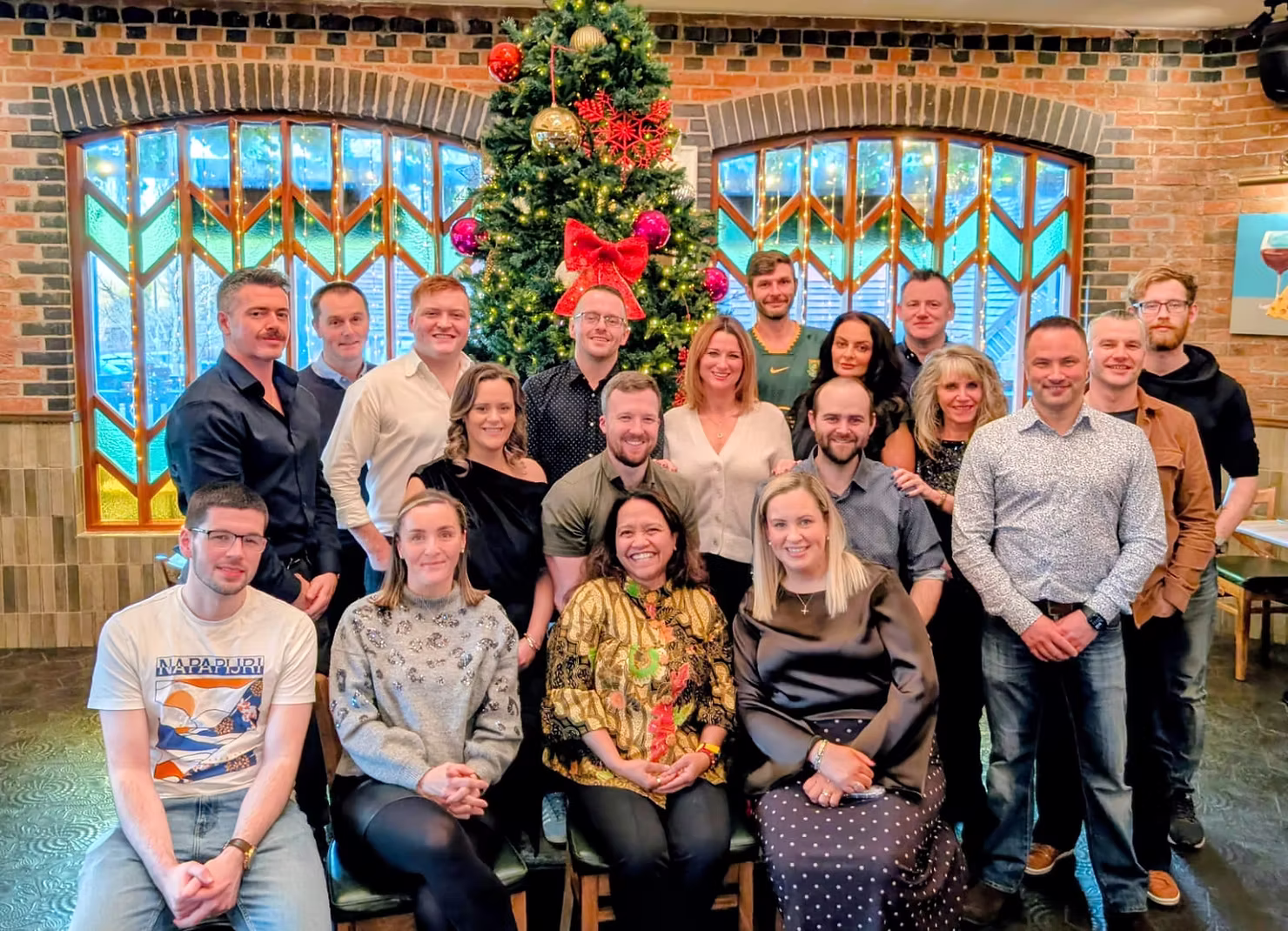 Team photo of employees gathered indoors in front of a decorated Christmas tree.