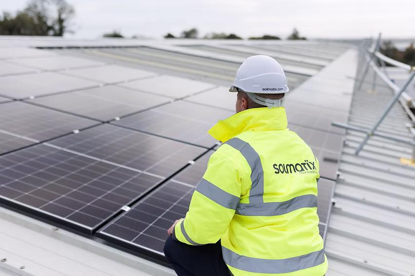 Solar installer wearing a high-visibility vest and hard hat working on a roof.