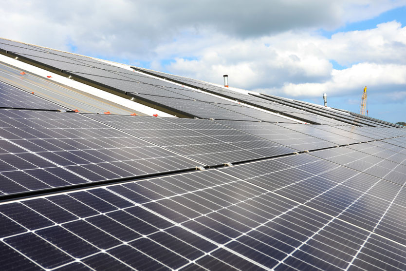 Low-angle perspective view along solar panels mounted on a light-colored roof.