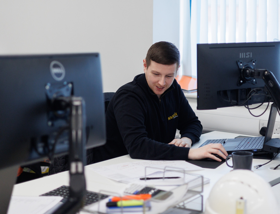A male colleague sitting together at a table discussing paperwork and looking at a computer.