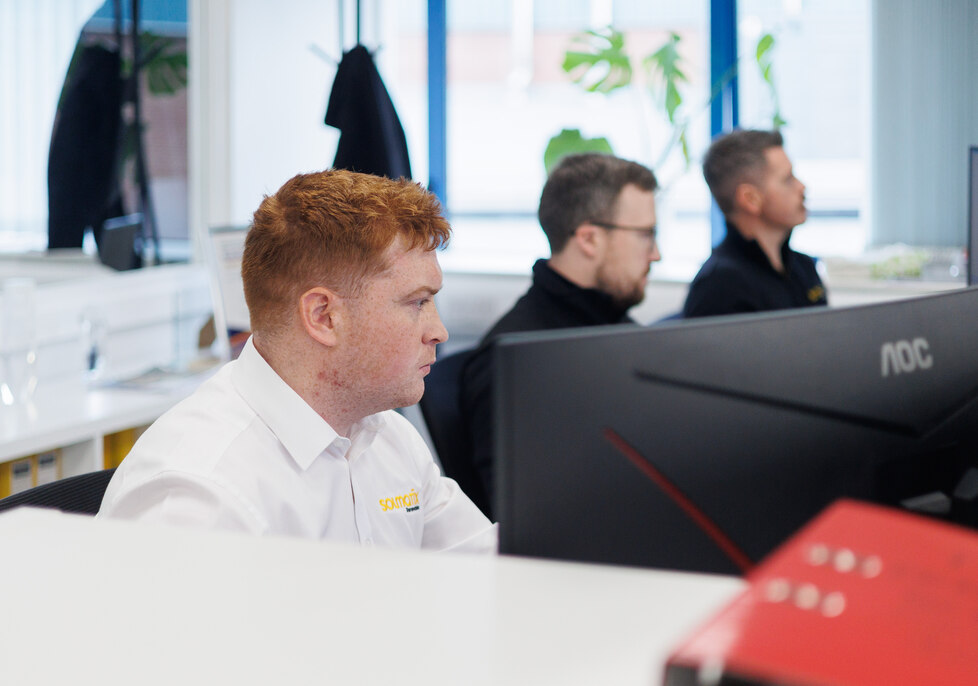 Three male colleagues sitting together at a table discussing paperwork and looking at a laptop computer.