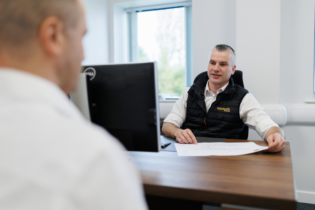 A male colleague sitting together at a table discussing paperwork with another male