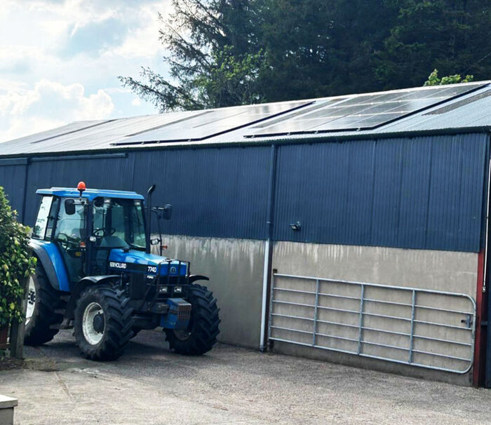 Blue tractor parked outside a large agricultural barn with rooftop solar panels.