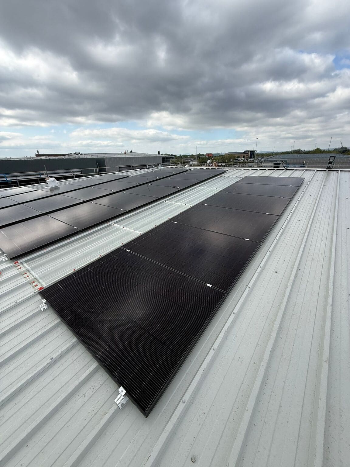 High-angle perspective view along solar panel arrays fitted between skylight panels on a commercial metal roof.