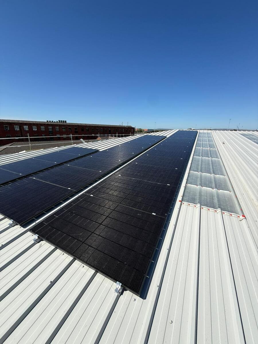 Perspective view along a continuous strip of solar panels fitted onto a corrugated metal commercial roof.