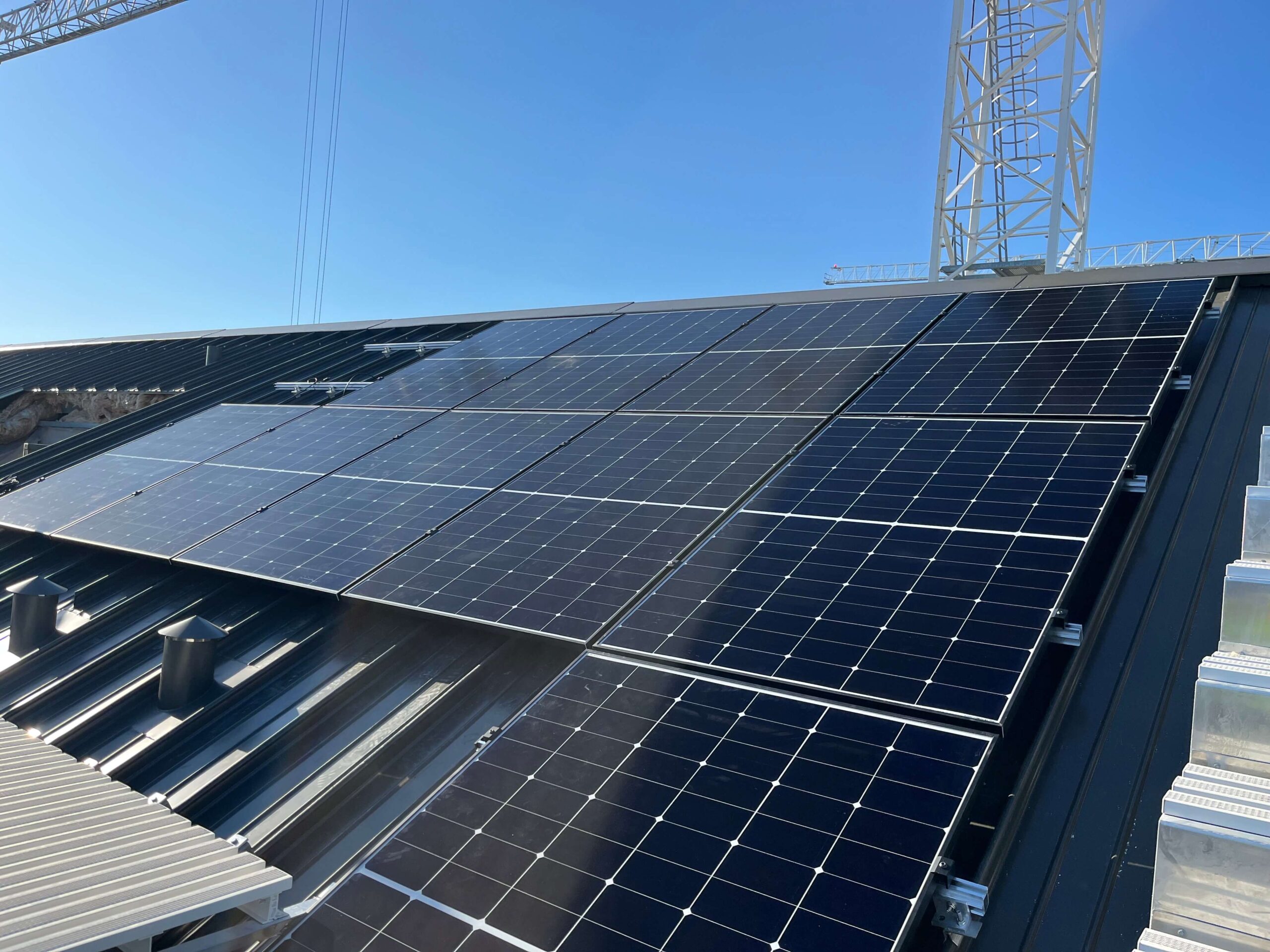 High-angle shot showing solar panels on a building roof with construction cranes in the distance.
