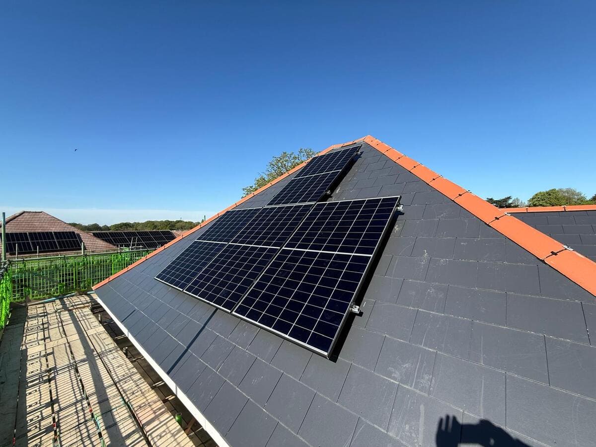 Solar panel modules installed across the tiled pitched roof of a residential house under a clear sky.