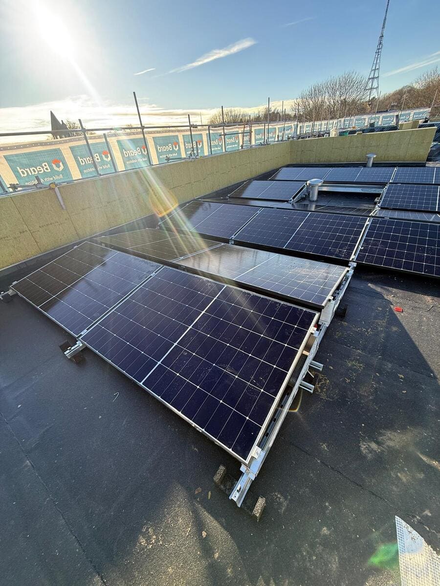 Angled rooftop solar panels set up on mounting frames on a flat roof under direct sun.