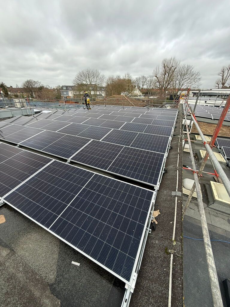 Perspective view down a wide row of rooftop solar panel arrays against an overcast sky.