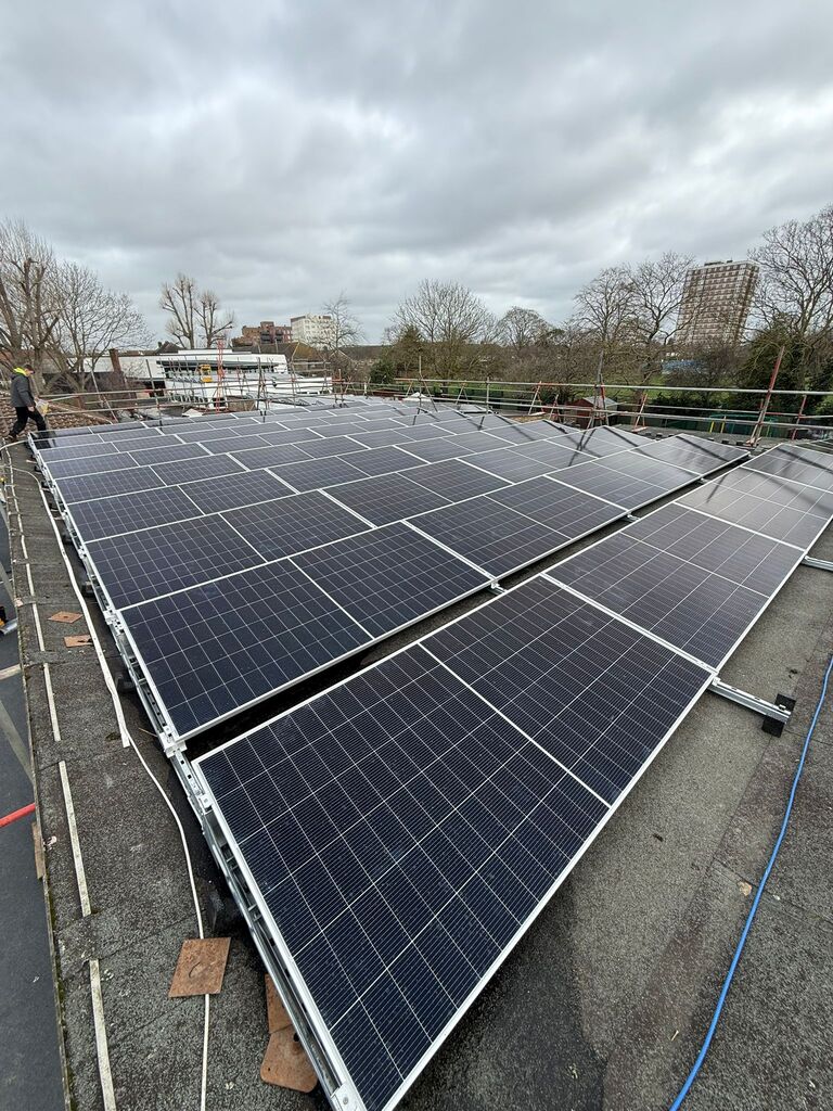 Perspective view down a wide row of rooftop solar panel arrays against an overcast sky.