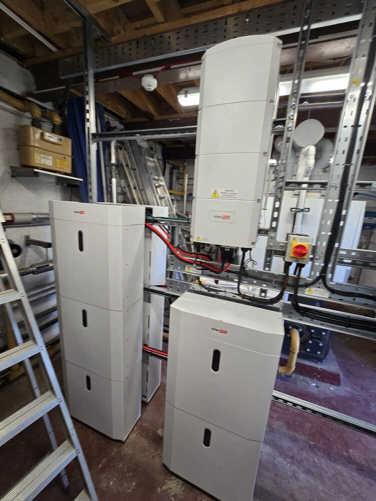 Wall-mounted solar inverters and electrical control boxes with conduit piping in an utility room.