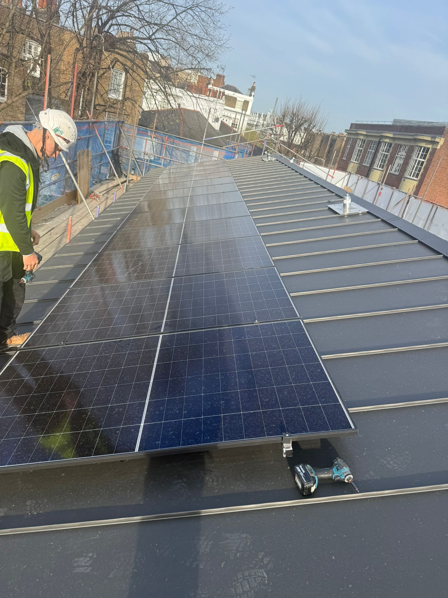 Installer in a high-visibility vest working near a rooftop solar array.