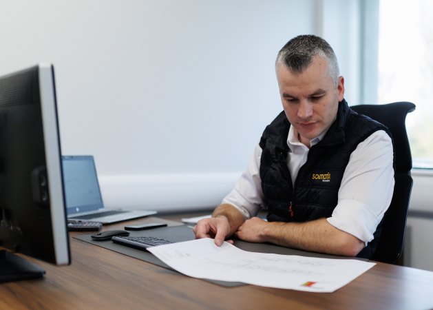 Man sitting at a desk reviewing documents in front of a open laptop.