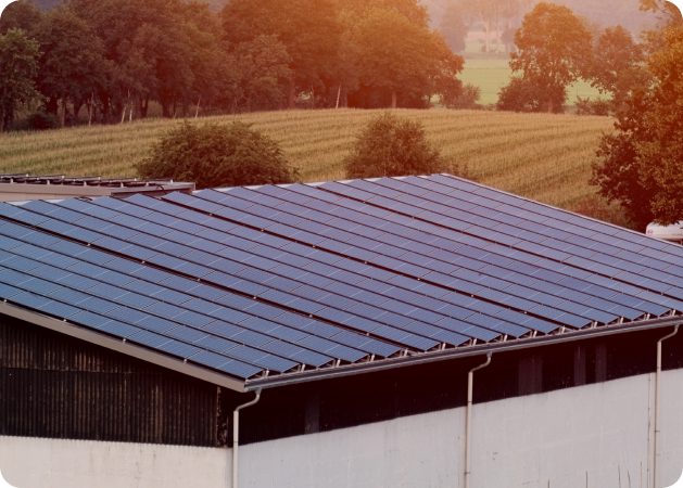 Rooftop solar panel installation on a corrugated farm roof overlooking rolling hills.