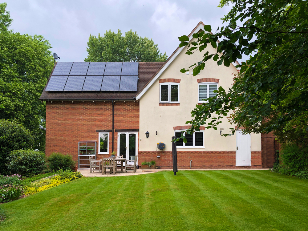 Solar panel array installed on the tiled pitched roof of a residential two-story house with a green lawn.