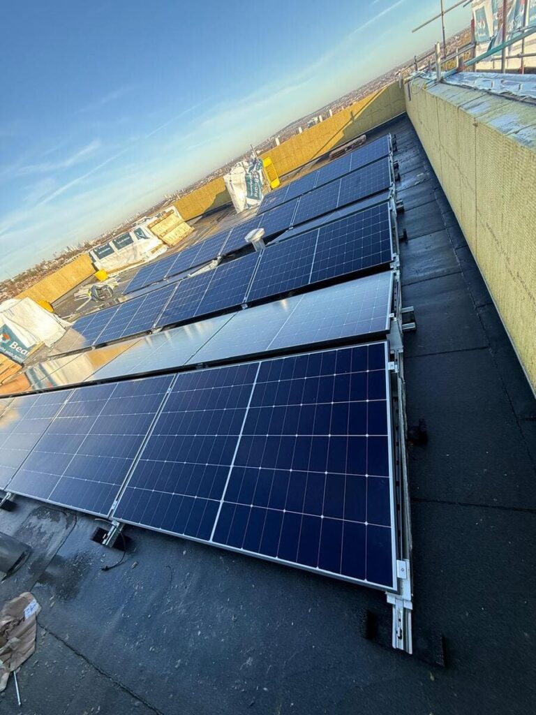 Low-angle perspective shot looking along flat-roof mounted solar panel arrays under a blue sky.