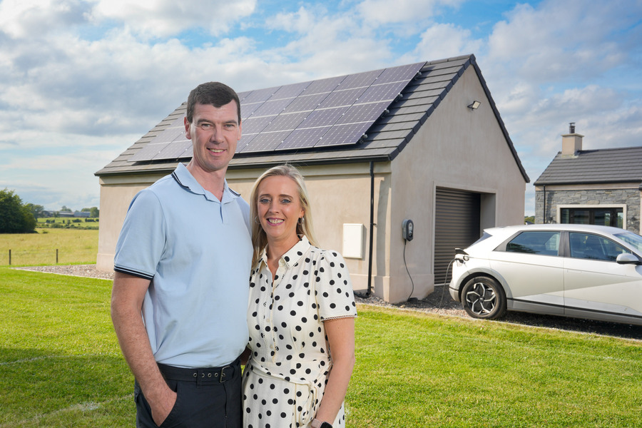 A couple outside their home with solar panels and electric car charging station